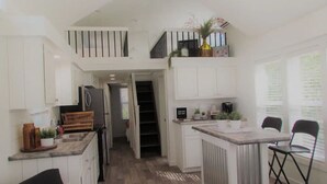 Eine moderne Küche mit einer zentralen Kochinsel, einem Essbereich mit Stühlen und einer Treppe, die in eine obere Etage führt.