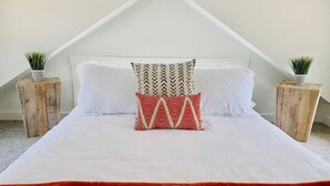 Ein Bett mit weißer Bettwäsche, einer roten Tagesdecke und zwei Blumentöpfen auf Nachttischen aus Holz.