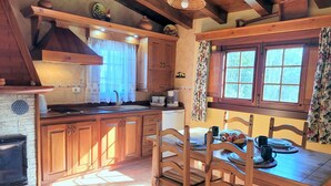 Une cuisine rustique avec des meubles en bois, une cheminée en pierre et un coin repas comprenant une table et des chaises en bois.