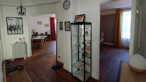 A spacious living room with a dining area, a glass display cabinet, and a clock on the wall. - Chez Michèle (Toul)