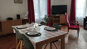A dining area with a table set for four, a television, and a bookshelf. - Chez Michèle (Toul)