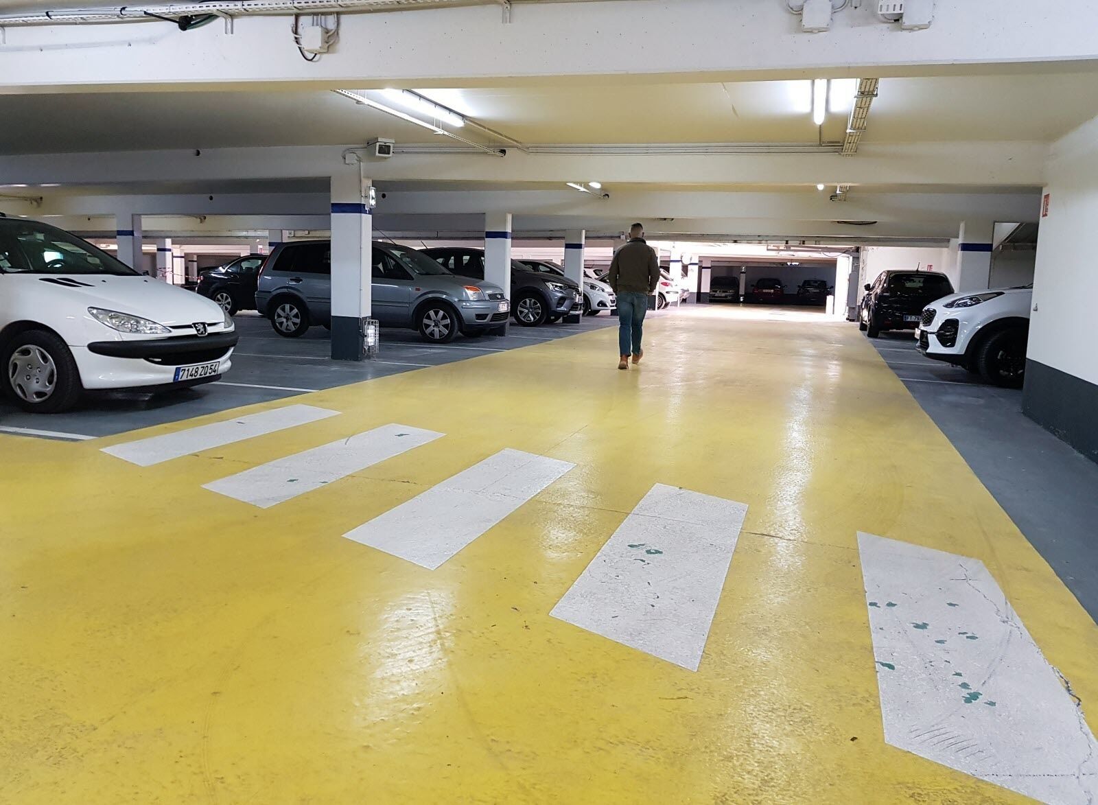 A multi-level parking garage with yellow and white painted lanes, multiple cars parked, and a person walking.