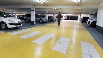 A multi-level parking garage with yellow and white painted lanes, multiple cars parked, and a person walking.