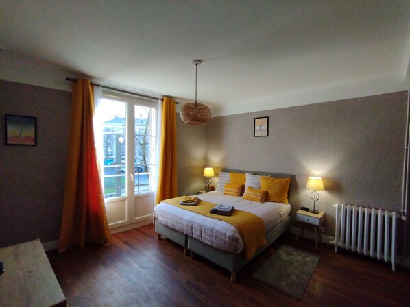 Une chambre à coucher avec un lit, des lampes de chevet, une fenêtre avec des rideaux, un radiateur et un tableau au mur.