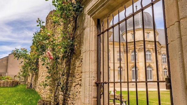 A historic building with a large arched window and a stone wall with climbing plants. - Chez Michèle (Toul)