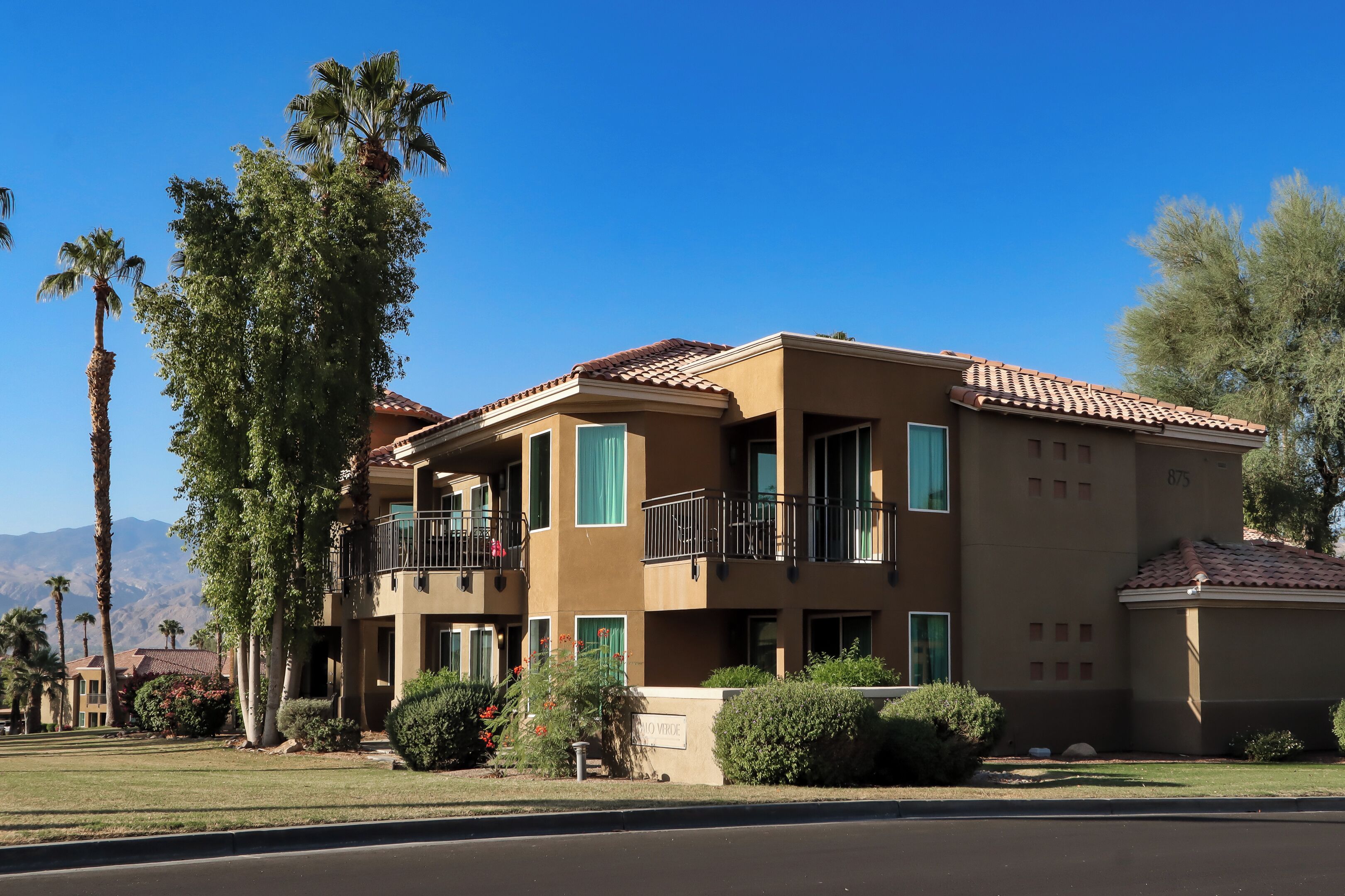 A multi-story residential building with balconies, a tiled roof, and a clear blue sky.