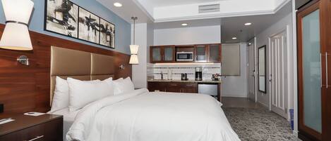 A hotel room with a large bed, a bedside table, a desk, a microwave, a coffee maker, and a wardrobe.