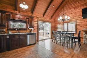 Cozy cabin-style room with a large kitchen area, dining space, and high ceiling with exposed beams.