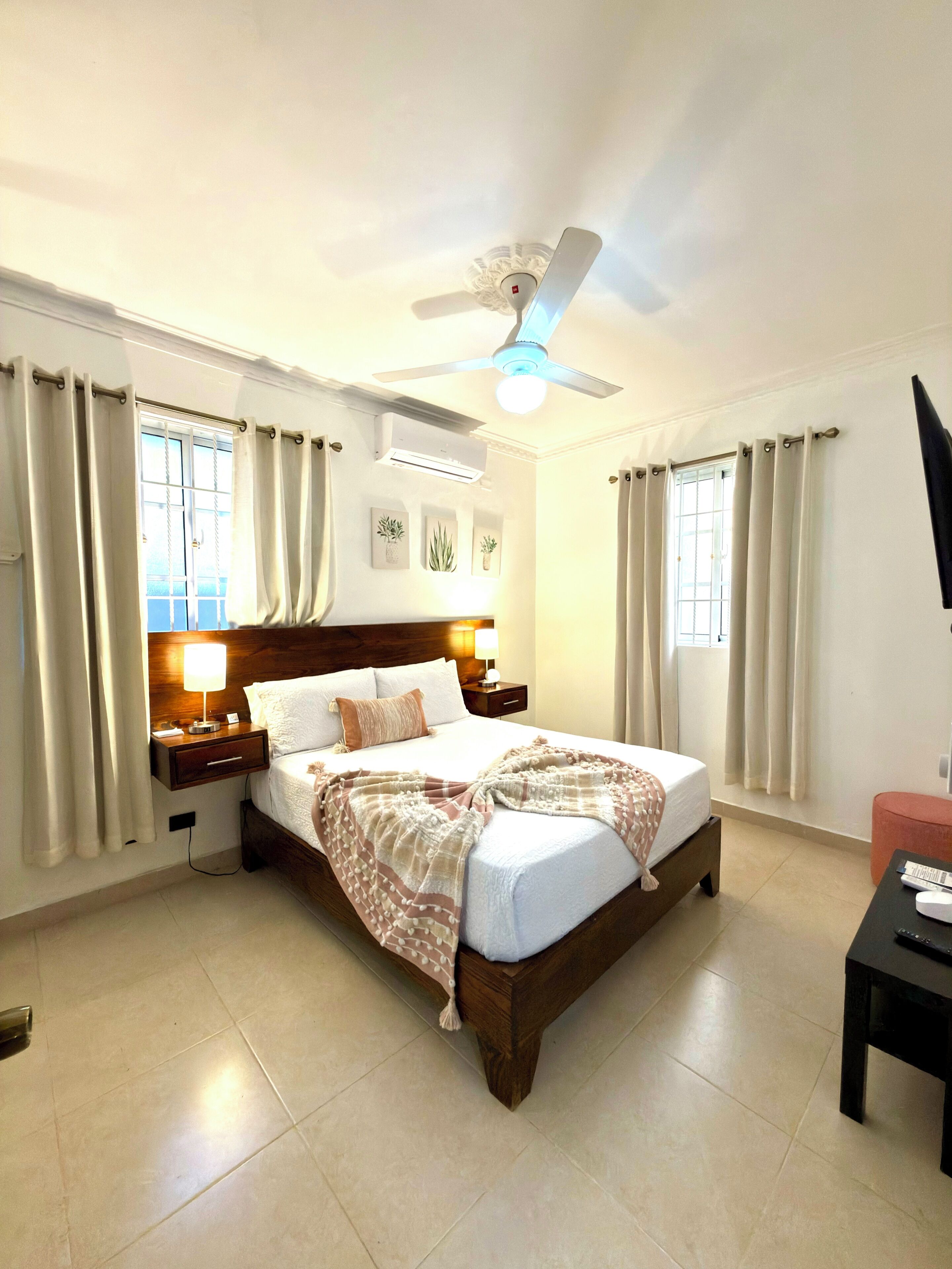 Een hotelkamer met een bed, nachtkastjes, een plafondventilator en een airconditioner.