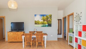 Ein Essbereich mit Korbstühlen, einem Holztisch und einem Fernseher auf einem Schrank.