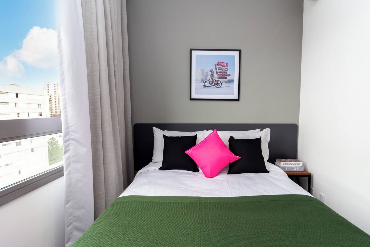 Une chambre d’hôtel avec un lit, un tableau encadré au mur et une fenêtre avec des rideaux.