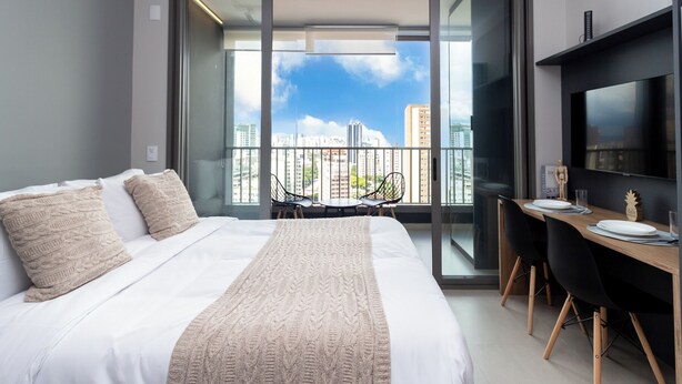 Ein modernes Hotelzimmer mit einem großen Bett, einem Essbereich und einem Balkon mit Blick auf die Stadt.