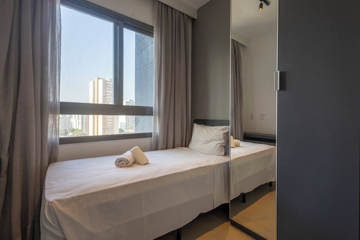 Une chambre d’hôtel avec un lit, une fenêtre avec des rideaux et un miroir.