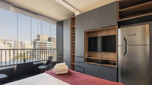 Ein modernes Hotelzimmer mit einem großen Bett, einem an der Wand montierten Fernseher, einem Kühlschrank und einem Balkon mit Blick auf die Stadt.