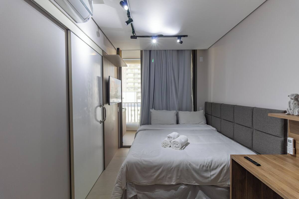 Une chambre d’hôtel moderne avec un lit bien fait, une table de chevet en bois et un téléviseur fixé au mur.