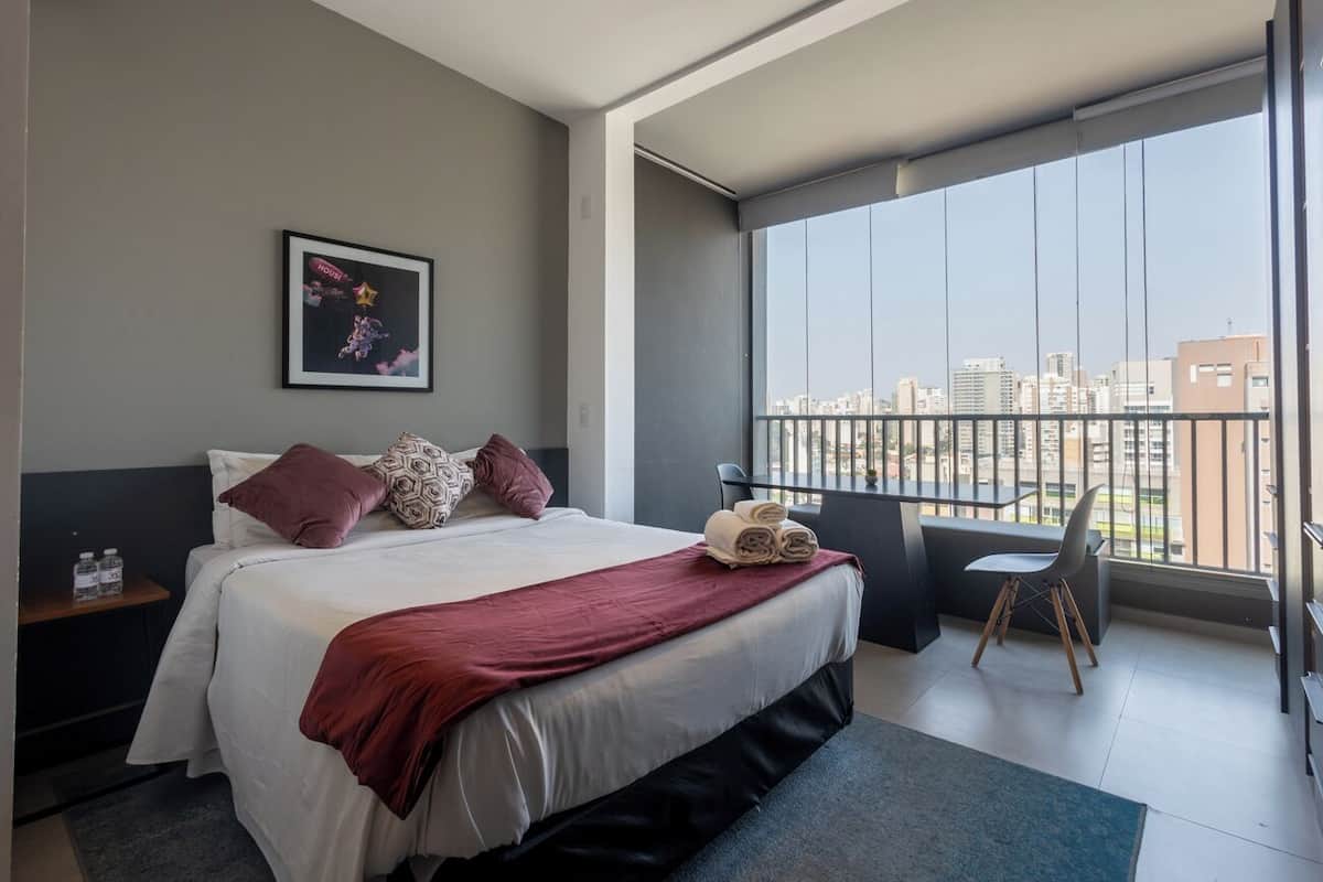 Une chambre d’hôtel avec un grand lit, un bureau et une vue sur la ville depuis un balcon.