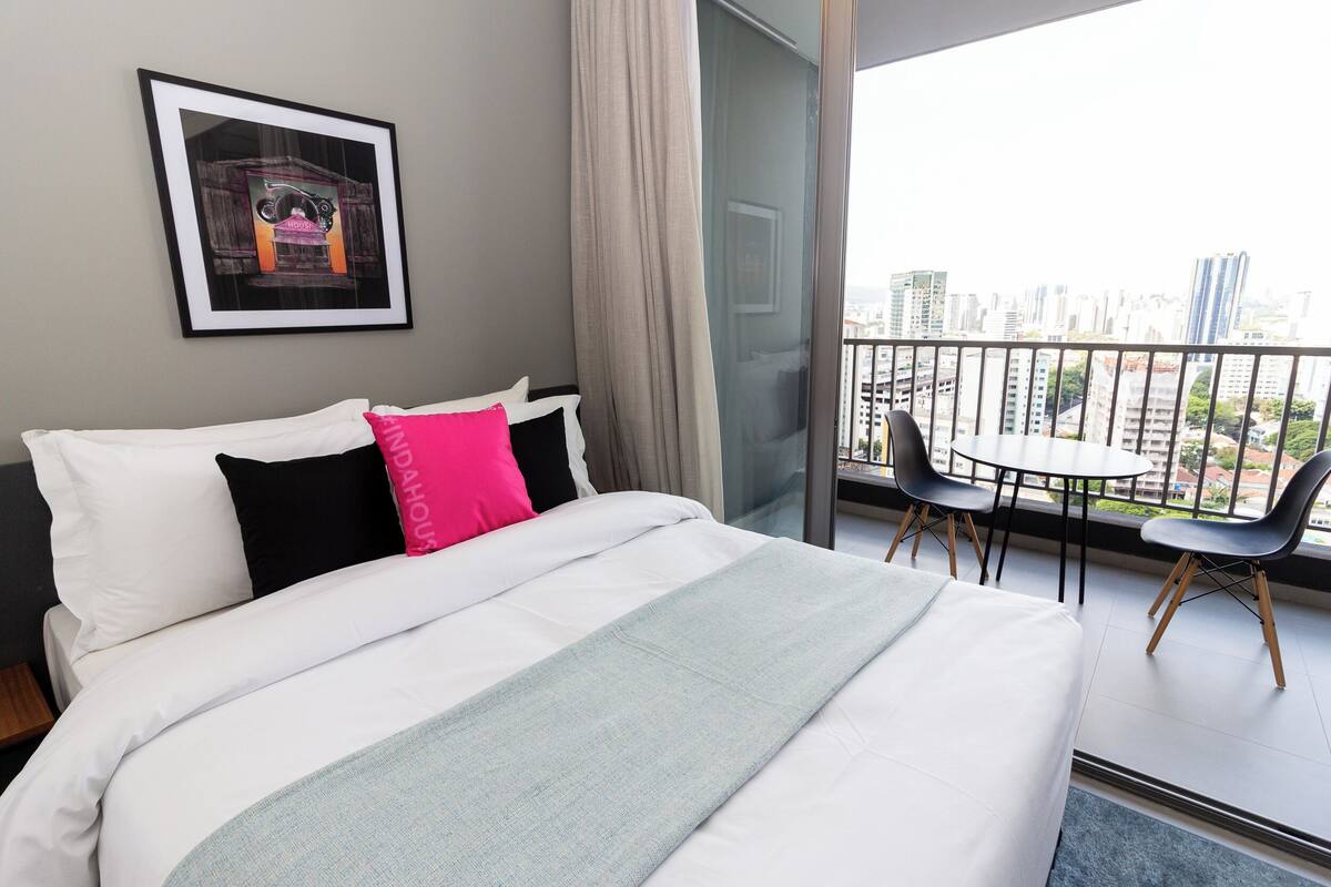 Une chambre d’hôtel avec un lit, un tableau encadré au mur, un balcon donnant sur la ville et une table avec des chaises.