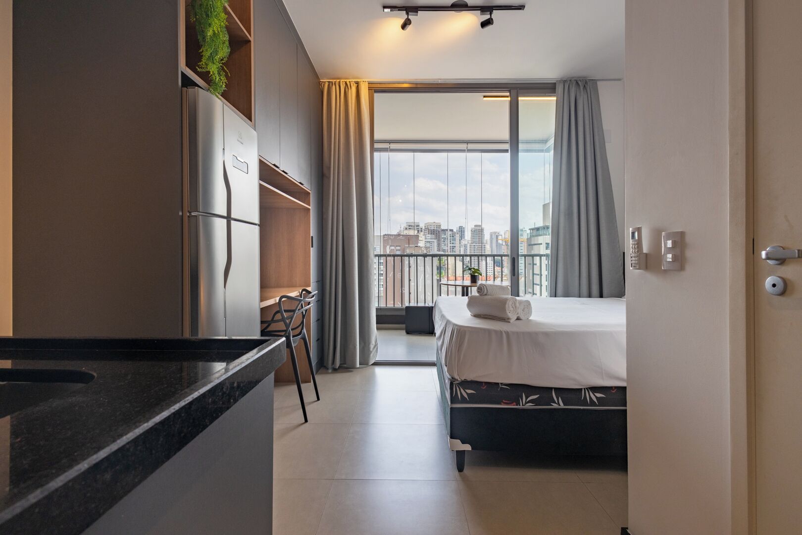 Moderni hotellihuone, jossa on parveke, sänky, työpöytä ja näkymä kaupunkiin.
