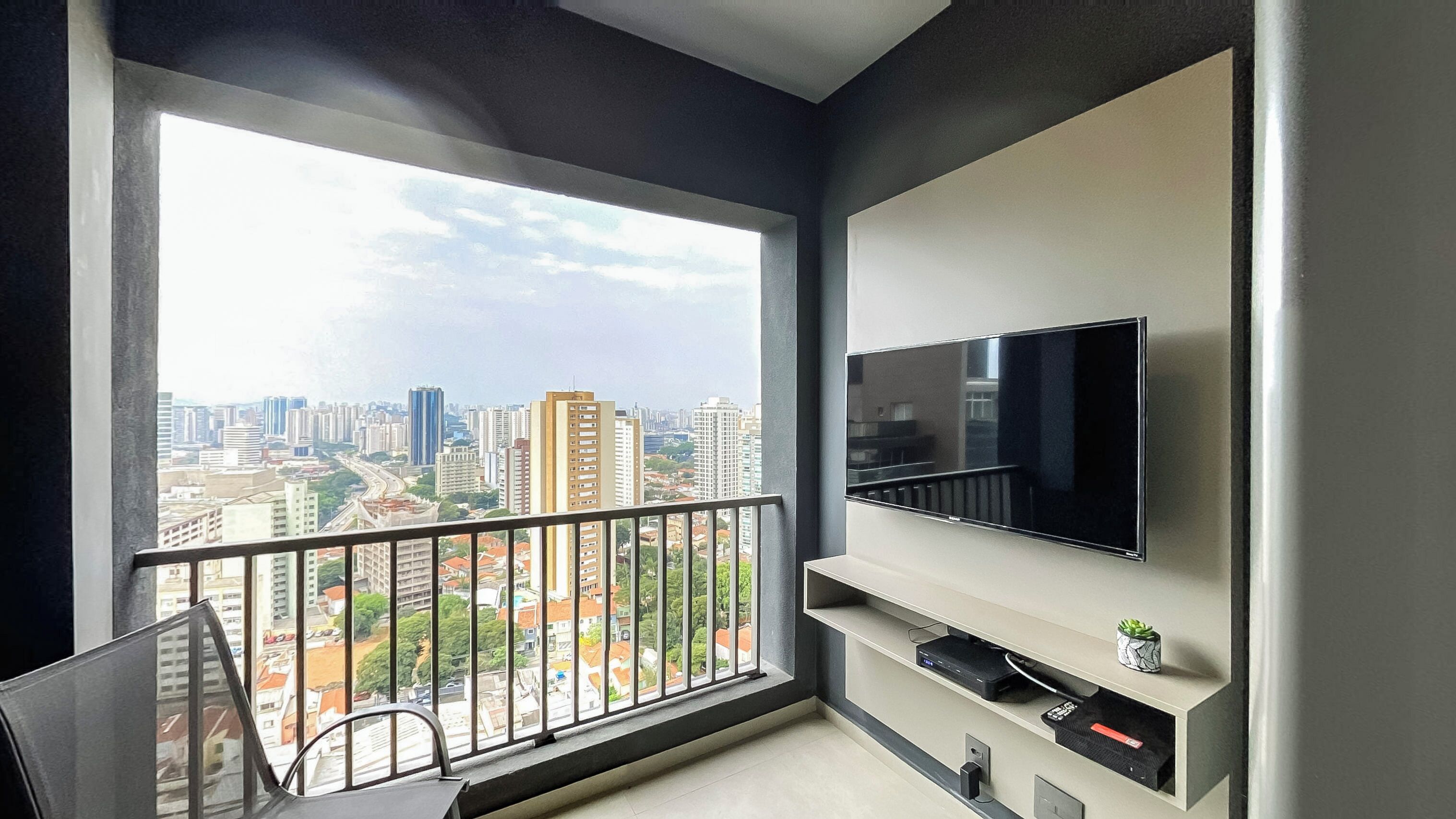 A modern apartment with a balcony, a TV mounted on the wall, and a city view.
