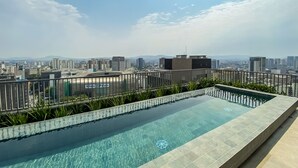Ein Infinity-Pool auf dem Dach mit Blick auf die Stadt, umgeben von einem Holzzaun und viel Grün.