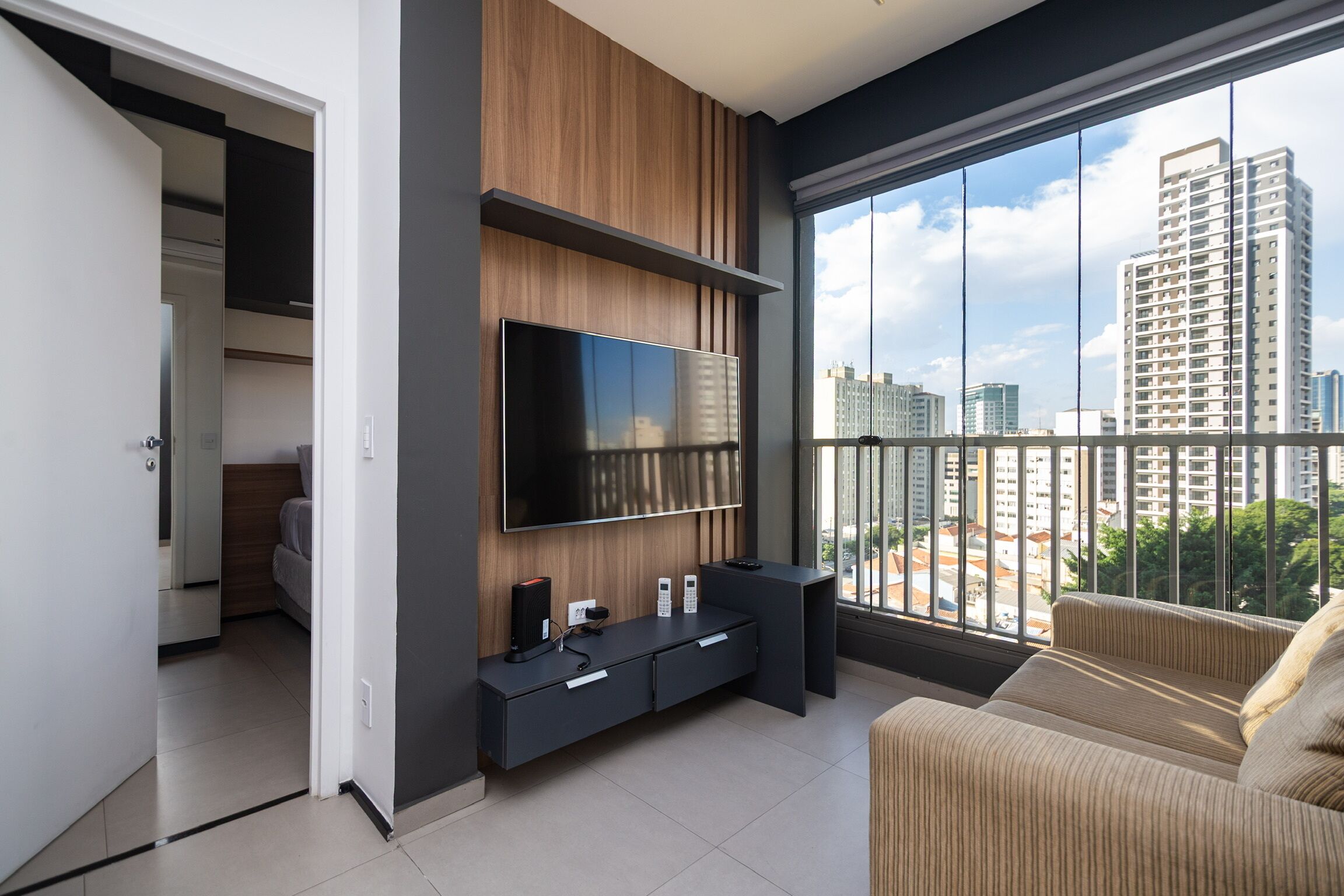 A modern living room with a large TV, a sofa, and a balcony with a city view.