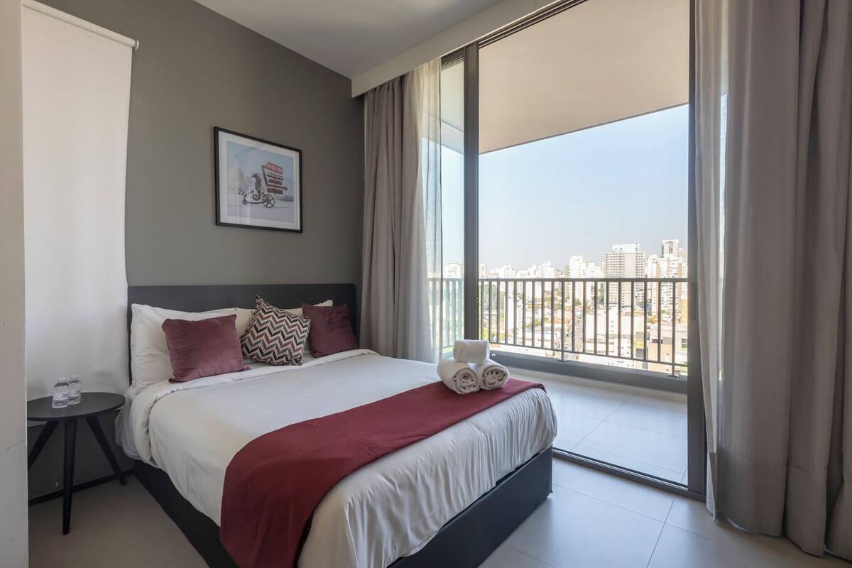 Une chambre d’hôtel avec un grand lit, un tableau encadré au mur et une vue sur la ville par la fenêtre.
