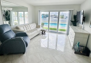 A modern living room with a sofa, a chair, a TV, and a view of a swimming pool. - Intracoastal living! (Pompano Beach)