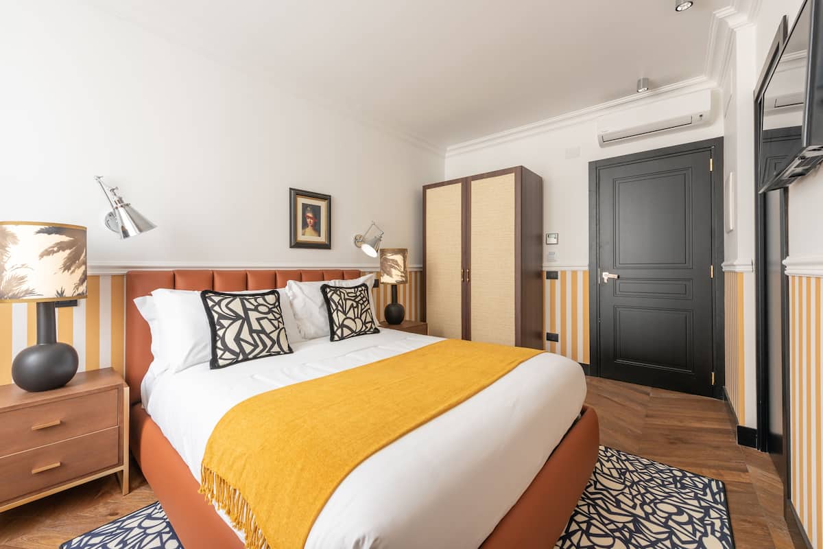 Habitación de hotel con una cama grande, una mesita de noche, una lámpara, un armario y una puerta.