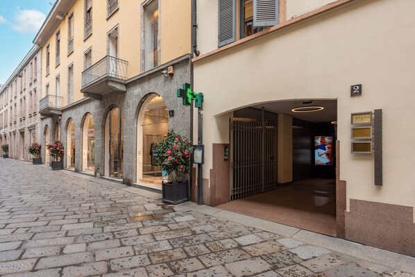 A cobblestone street with a hotel entrance, a green cross sign, and a number '2' sign. - HÕMA Spiga (Milan)
