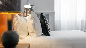 En pænt redt seng med hvidt sengetøj, en sort lampe på et trænatbord og en pude med sort-hvidt mønster.
