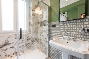 A bathroom with a glass shower enclosure, a white sink, and a tiled backsplash. - HÕMA Spiga (Milan)