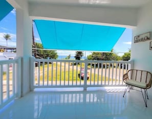 A balcony with a blue awning, white railing, and a wicker chair.
