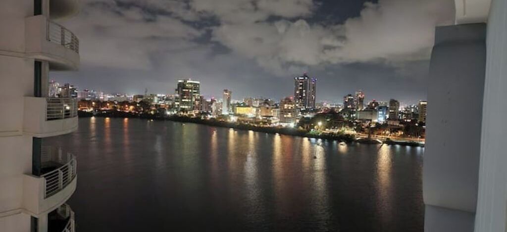 A nighttime cityscape with buildings along a waterfront.