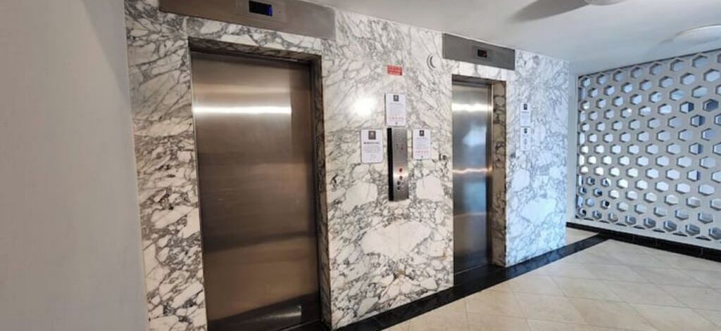 Zona d'ascensor amb parets de marbre i porta metàl·lica.