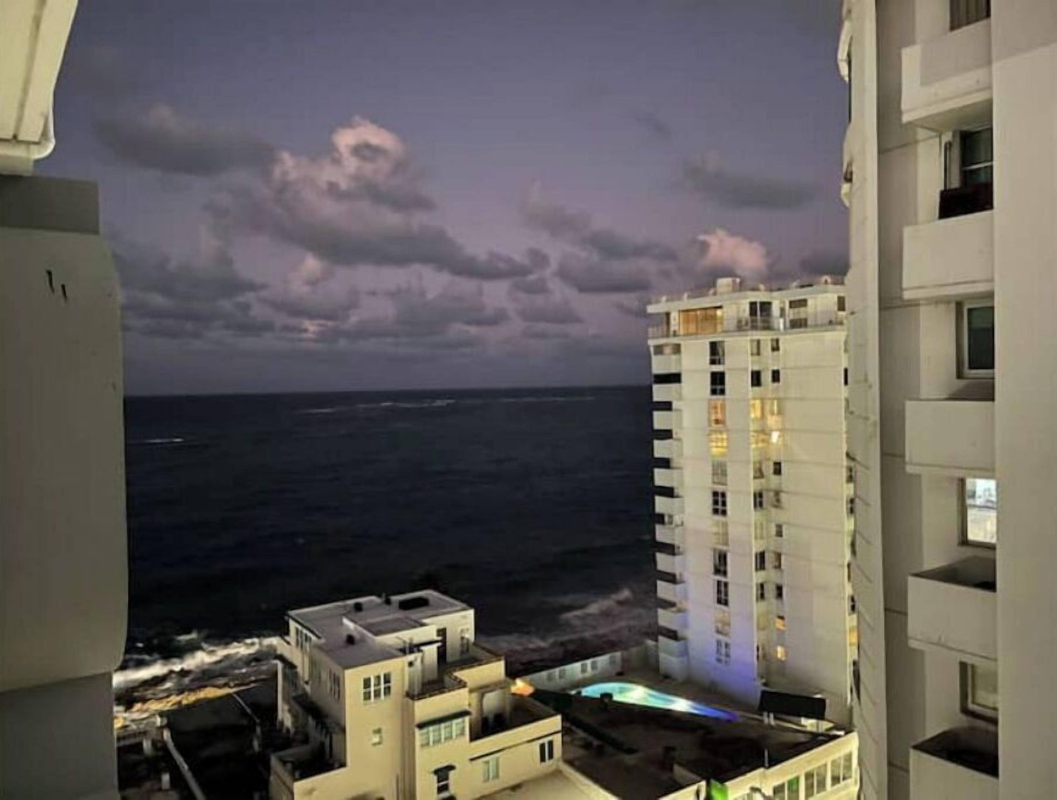 A high-rise building with a pool on the rooftop, overlooking a body of water.