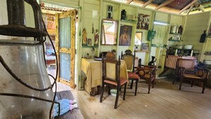 Een rustiek interieur met houten meubels, een eettafel en diverse decoraties, waaronder religieuze beeldjes en een grote spiegel.
