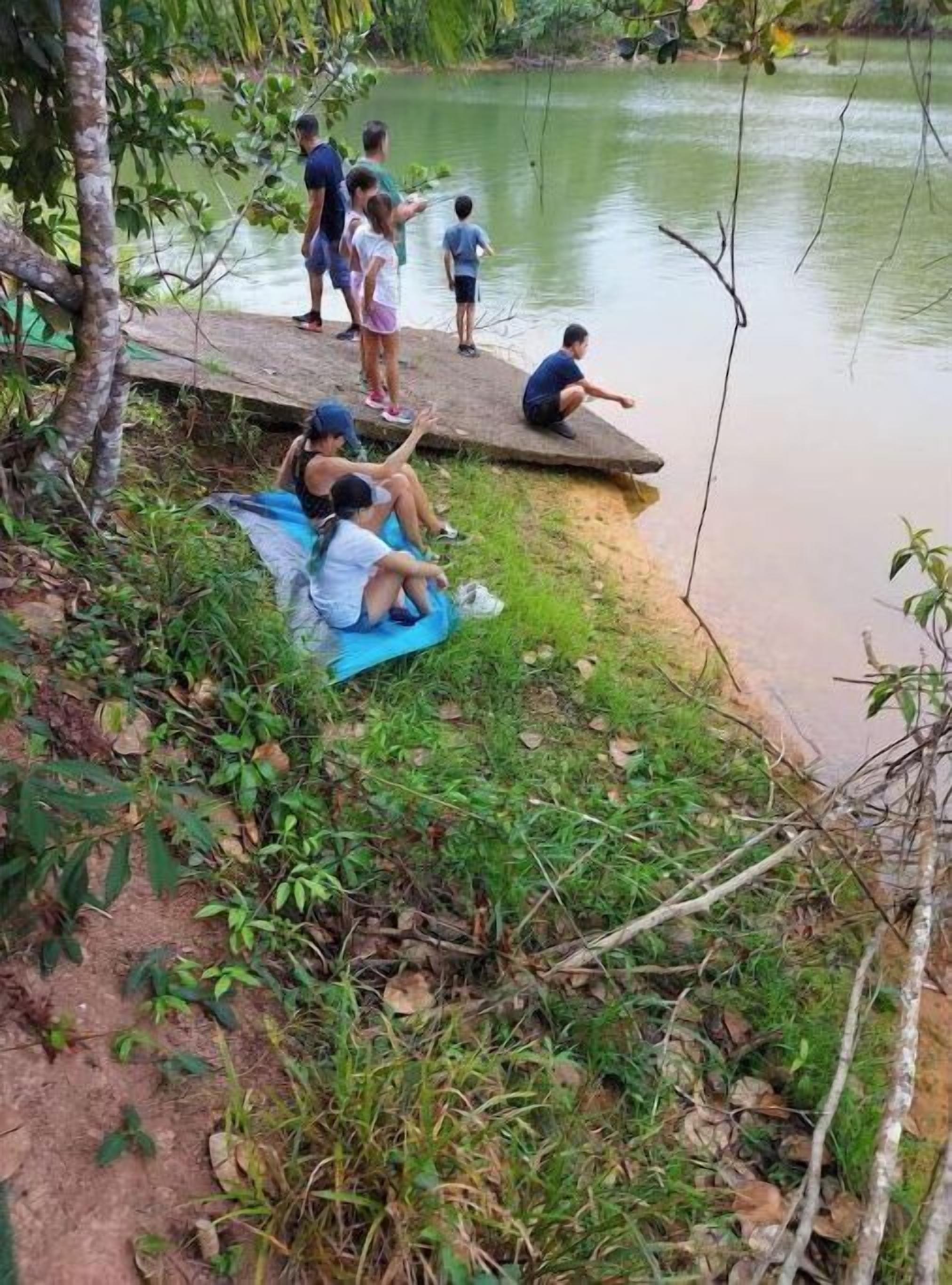 Un groupe de personnes se détend au bord d’une rivière, certaines assises sur un tapis, d’autres debout.