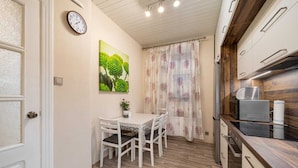Una cucina compatta con zona pranzo, con un orologio, un quadro e una tenda.