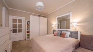 Una camera da letto con un letto grande, un armadio, una libreria a muro con libri e giocattoli, e uno specchio.