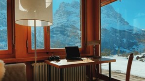 A cozy room with a wooden desk, a laptop, and a chair, overlooking a snowy mountain landscape through large windows. - Alpine Escape - Iconic Views & Timeless Design (Grindelwald)