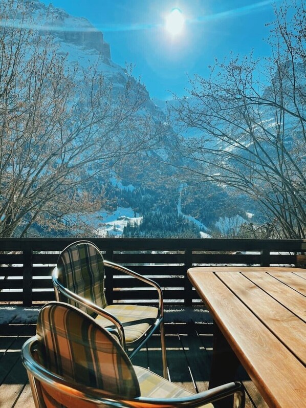 A wooden table and two chairs with a view of a mountainous landscape.