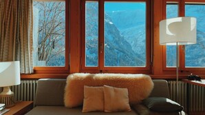A cozy room with a sofa, pillows, a lamp, and a view of mountains through large windows. - Alpine Escape - Iconic Views & Timeless Design (Grindelwald)