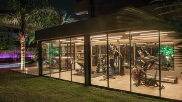 A modern gym with glass walls, various exercise equipment, and a pool area visible outside.