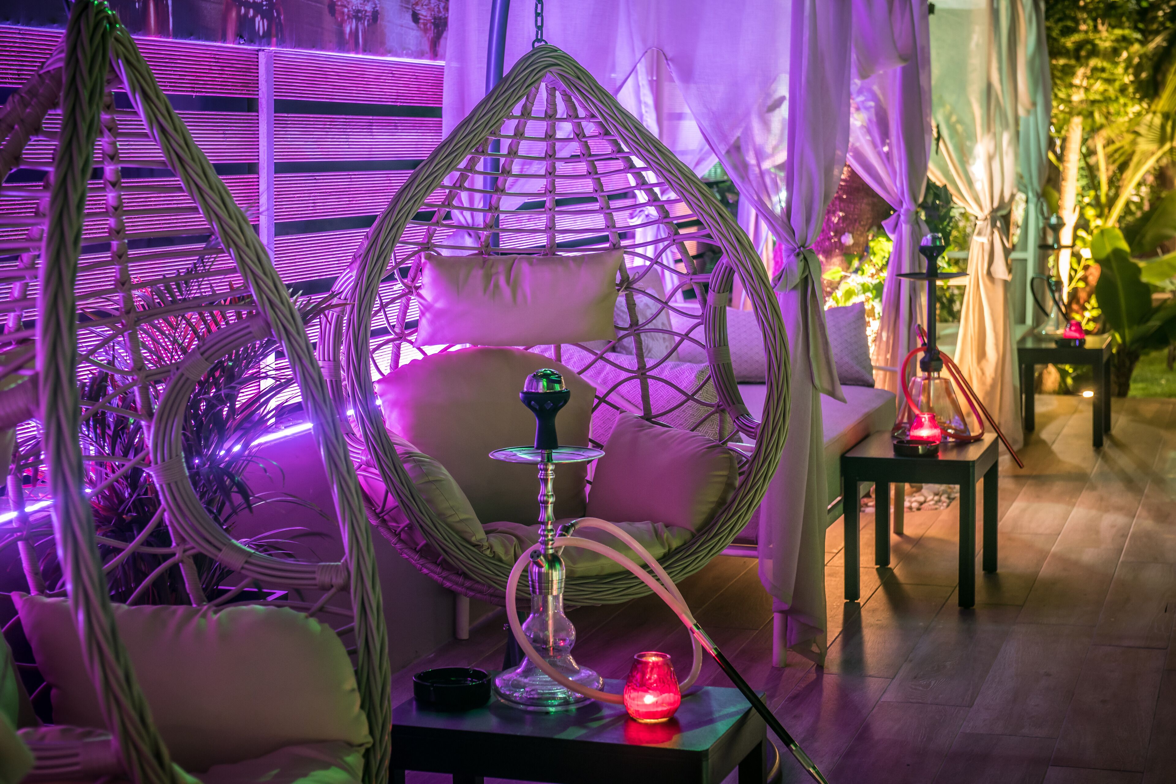 Una habitación con una silla colgante, una mesa con un narguilé y una mesita con una vela.