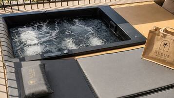 Un espace bien-être comprenant un jacuzzi, des chaises longues et un sac orné du logo de l’hôtel.