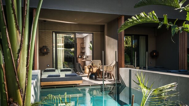 A modern outdoor pool area with a seating area, lounge chairs, and a glass-enclosed room with a bed.