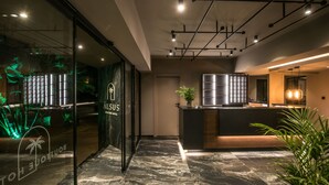 A modern hotel lobby with a reception desk, a glass wall with illuminated palm tree design, and a marble floor.