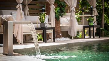 A poolside area with a water feature, outdoor seating, and greenery.