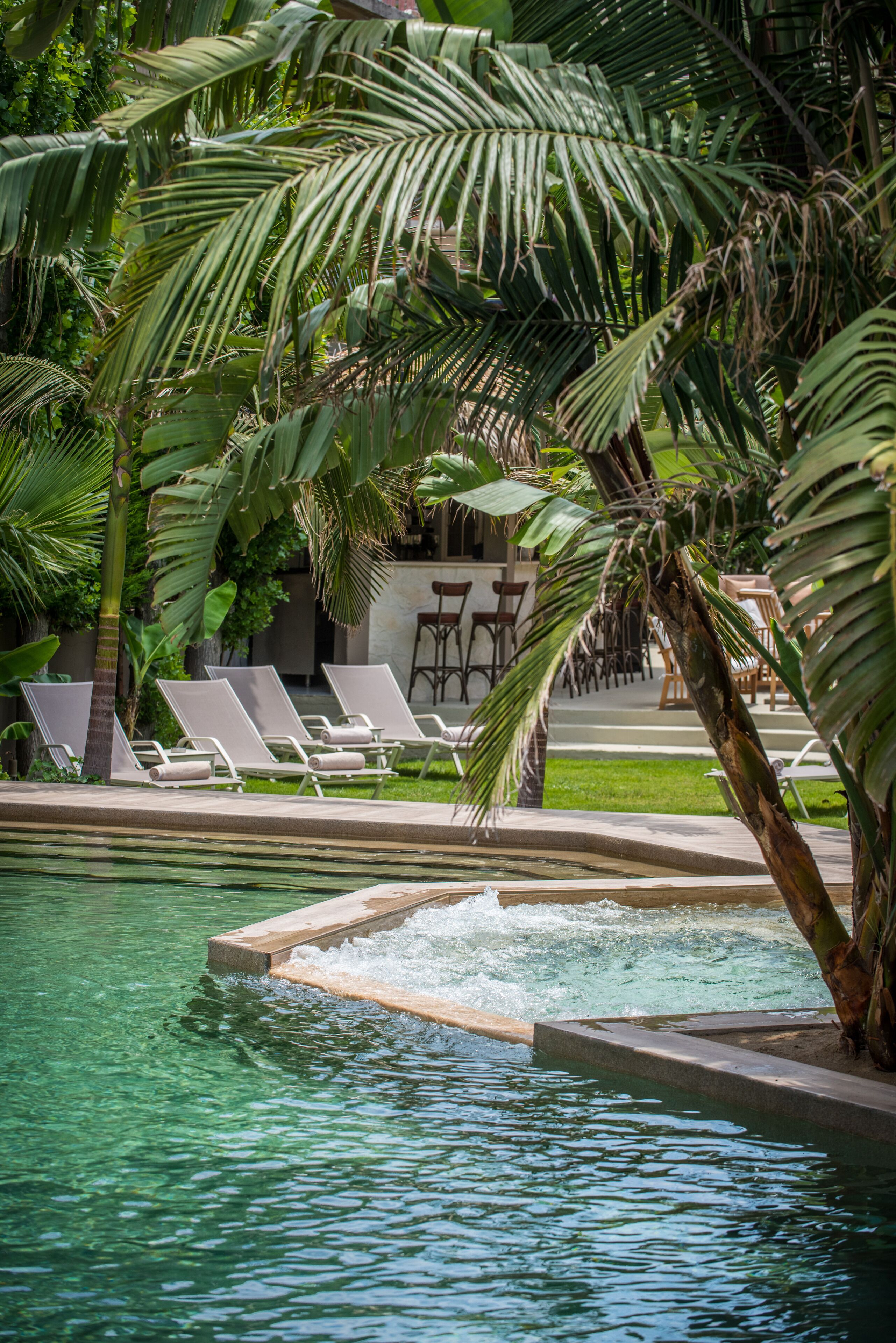 A pool area with lounge chairs, a small waterfall feature, and surrounding tropical vegetation.