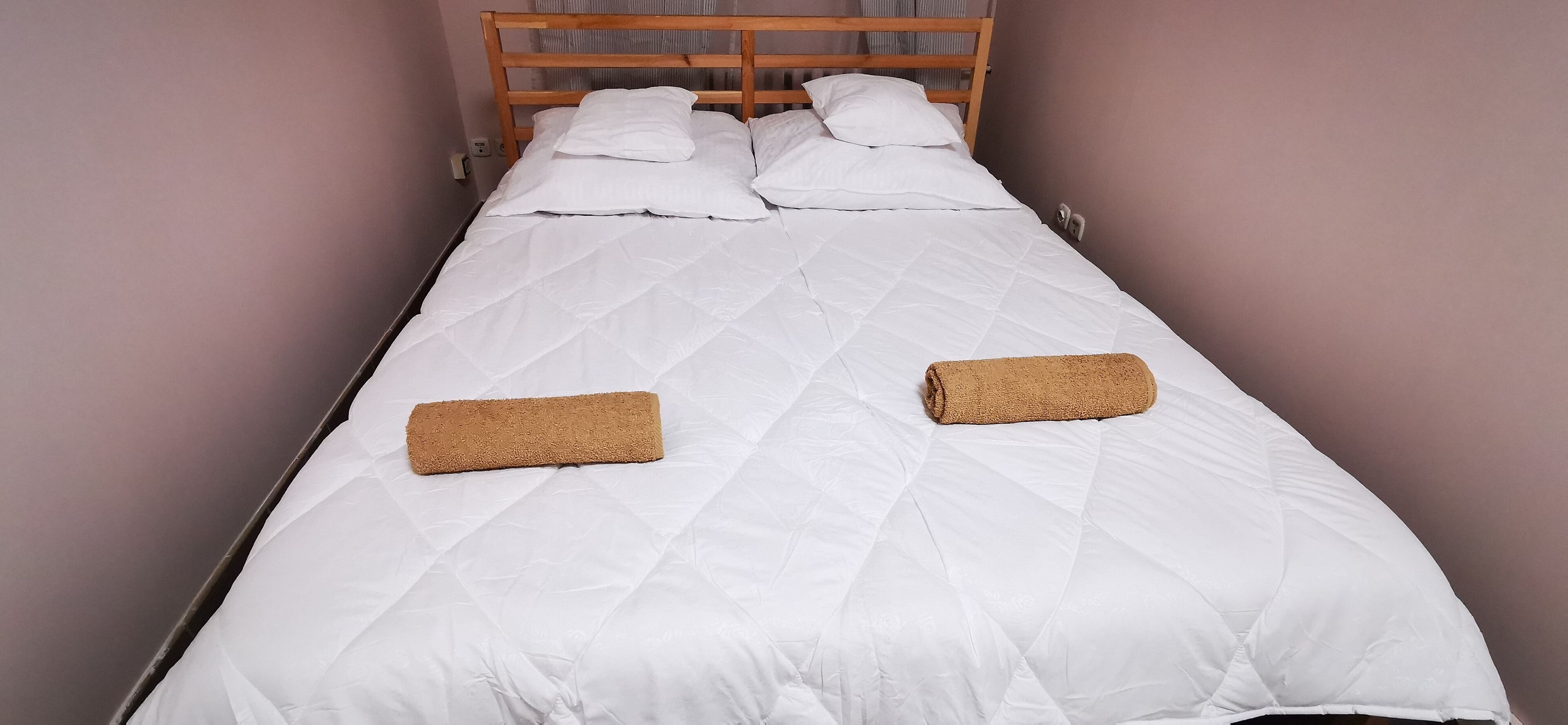 A single bed with a wooden headboard, white bedding, and two rolled towels.